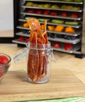 Top Shelf Eight Tray Stainless Steel Food Dehydrator with homemade beef jerky in jar next to fresh strawberries.