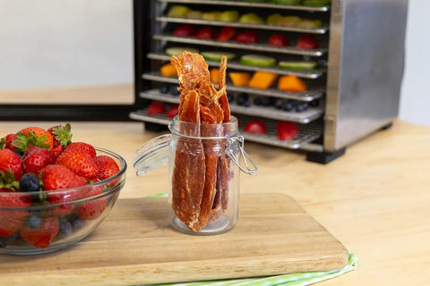 Top Shelf Eight Tray Stainless Steel Food Dehydrator with homemade beef jerky in jar next to fresh strawberries.