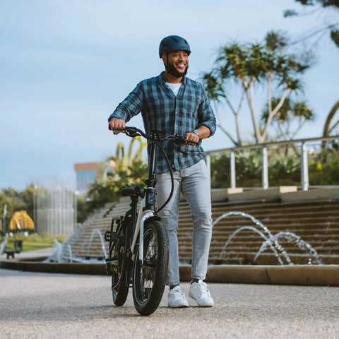 Person walking with a fat tire bike near a park fountain.