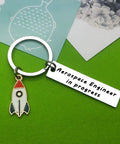 Funny Aerospace Engineer Keychain Gift For Graduation And Appreciation with rocket charm on green surface