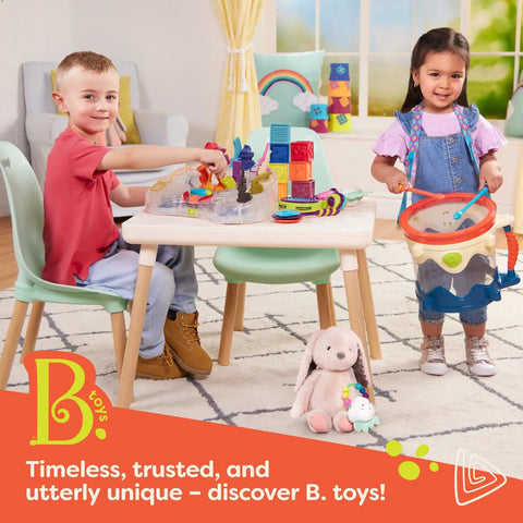 Two toddlers playing with B. toys on a table, including blocks and a drum, in a colorful playroom with plush animals.