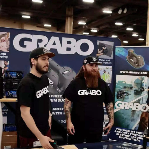 Grab On Pro Electric Suction Cup Lifter demonstration at a trade show with two men showcasing the portable heavy-duty tool.