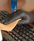 Black nitrile disposable glove wiping a computer keyboard with an orange cloth
