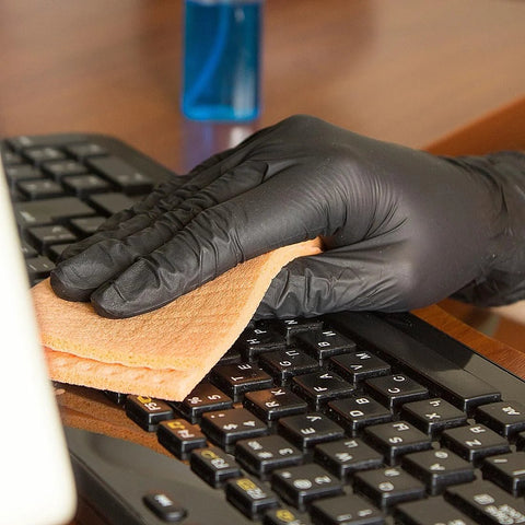 Black nitrile disposable glove wiping a computer keyboard with an orange cloth