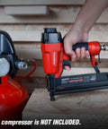 Hand holding 18 Gauge Pneumatic Brad Nailer And Crown Stapler 2 In 1 Nail Gun connected to air compressor on wood surface