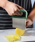 Crinkle cutter with green handle, stainless steel ribbed blade slicing a potato on a plate