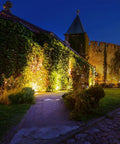 JUDYSSY Solar Flood Lights Led Solar Light illuminating an ivy-covered wall near a castle at night.