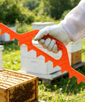 Beekeeping Frame Spacers 2 Pack 9 Frame Spacer Tool For Beehive Boxes, orange tool in gloved hand, beehives in background.