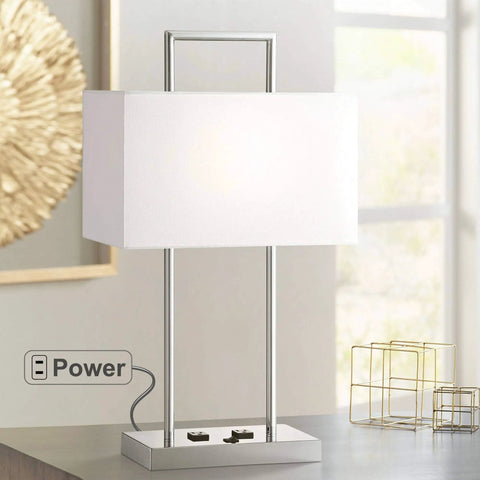 Jaymes Chrome Table Lamp With White Fabric Shade, 26-Inch Tall on desk, showing power outlet feature