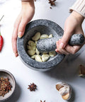 Hand using granite mortar and pestle set for grinding spices and herbs like a boss, natural non porous stone, garlic inside
