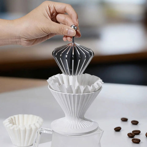 Hand placing reusable stainless steel filter into white pour over coffee dripper cup. Solid 3 In 1 Metal Pour Over Coffee Dripper Gift Set With Reusable Stainless Steel Filter And 25 Basket Papers For Hassle Free Brewing Smooth Daily Grind Or Chill Travel Vibes At Home And On The Road.