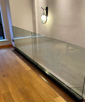 Heavy Duty Glass Railing System For Deck And Balcony Featuring Rock Solid Spigot Clamps With Flexible Floor Or Side Mount Hardware And Premium Aluminum Posts In Matte Black Covers For Quick Pool And Yard Fence Projects showcased indoors with wooden floor.