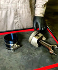 Mechanic with adjustable piston ring compressor tool fits 3.5 to 7 inch pistons, spring steel body on workbench.