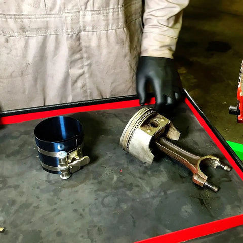 Mechanic with adjustable piston ring compressor tool fits 3.5 to 7 inch pistons, spring steel body on workbench.