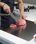 Front view of a stainless steel kitchen cutting board being used to slice raw beef with a chef knife.