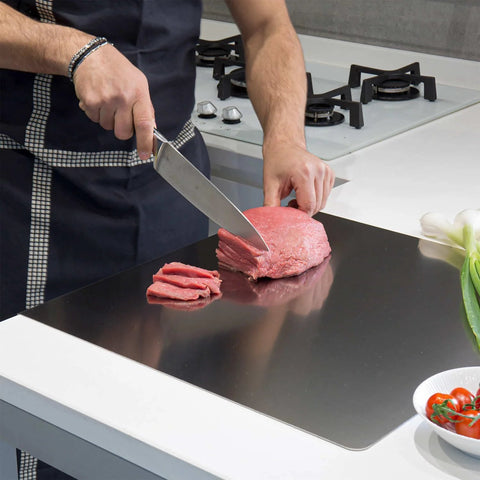 Front view of a stainless steel kitchen cutting board being used to slice raw beef with a chef knife.