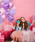Two girls wearing masks with Sixty Eight Piece Pink And Purple Balloons Set 12 Inch Metallic Latex Party Decor for celebration.