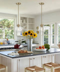 MQMQA 2 Pack Globe Pendant Lights, Mid Century Brass Pendant Light Fixtures over a kitchen island with sunflowers and fruit.