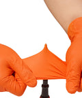 Hands wearing Tough As Nails Industrial Orange Nitrile Work Gloves With Solid Eight Mil Thickness and Raised Diamond Texture stretching the glove.
