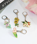 Five floral enamel pin keychains on silver metal, featuring sunflower, pink tulips, purple irises, and bouquet with bow