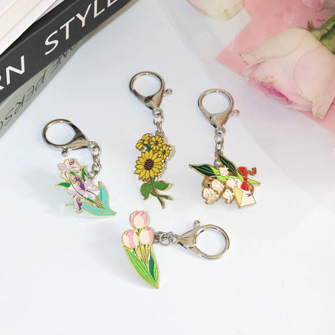 Five floral enamel pin keychains on silver metal, featuring sunflower, pink tulips, purple irises, and bouquet with bow