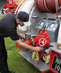 Person polishing fire truck equipment outdoors with metal cleaner, showing hoses and gauges, on grass field.