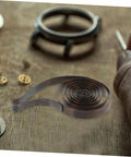 Mechanical clock spring for alarm clocks DIY repairs and craft projects replacement component on wooden table with clock parts.
