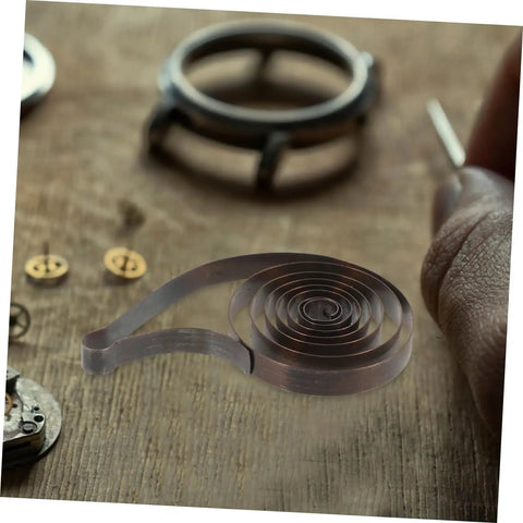 Mechanical clock spring for alarm clocks DIY repairs and craft projects replacement component on wooden table with clock parts.