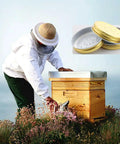 Beekeeper with Ten Pack Metal Bee Entrance Feeders 2.87 Inch For Beehives, Durable Water Feeder Lids next to a wooden beehive