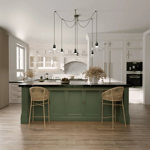 Modern kitchen with green island, two rattan chairs, and pendant lighting, featuring light wood flooring and white cabinetry.