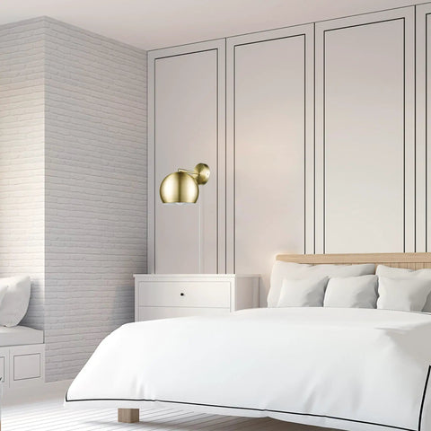 One Light Plug In Or Hardwire Wall Sconce With Vintage Glam Matte Brass Finish in bedroom setting with white walls.