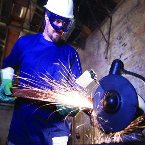 Odyssey II Eye Protection Goggles for Work worn by man grinding metal, anti fog, scratch resistant, latex free, blue frame.