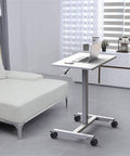 Fully Adjustable Rolling Laptop Stand With Rugged Aluminum Frame Convertible Standing Desk Tray beside a white couch in a modern living room.