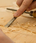 Close-up of a hand carving wood with a chisel, showcasing precise woodworking techniques for CNC projects.