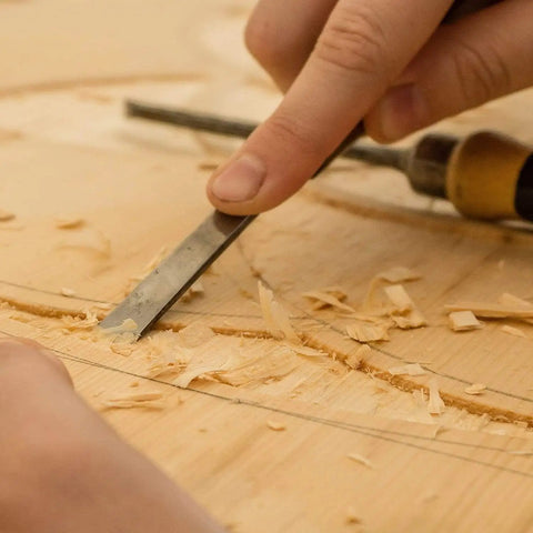 Close-up of a hand carving wood with a chisel, showcasing precise woodworking techniques for CNC projects.