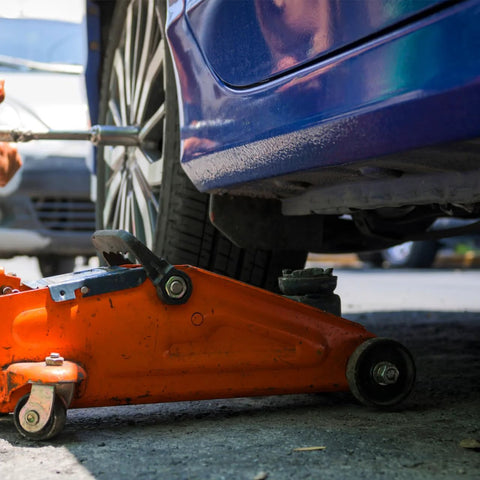 Orange hydraulic floor jack lifting a blue car using Front Wheel Replacement For Two And A Half Inch Iron Wheel For Two Ton Hydraulic Floor Jacks Heavy Duty Pro Grade Universal Roller Accessory With Professional Bearing For Horizontal Jack And RV Stabilization.