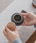 Person holding a snug wooden lid and a heavy ceramic tea jar with loose tea, part of the set to kick up your pantry game.