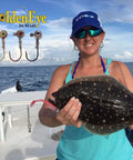 Woman on boat holding flounder with GoldenEye Jig Heads displaying inshore jig head for soft plastics with red eye and red hook.