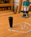 Score Your Shop Upgrade With This Six By Nine Inch Clear Acrylic Router Base Plate Built Straight For Makita Compact Models Featuring Pre Drilled Mounting Holes And Three Eighth Inch Thickness For Rock Solid Precision Woodworking on a wooden table with a router.
