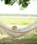 Handmade Boho Macrame Fringe Double Hammock Swing Net Chair For Two People Ultra Cozy Outdoor Indoor Patio Beach Yard Decor 95 Inches By 59 Inches Heavy Cotton Blend For Extra Comfort And Durability hung outdoors with a child inside