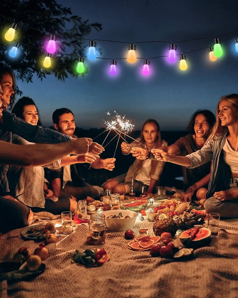 Smart RGB Outdoor String Lights 96ft With Independent Bulb Color Control illuminating a picnic scene with vibrant colors at night.