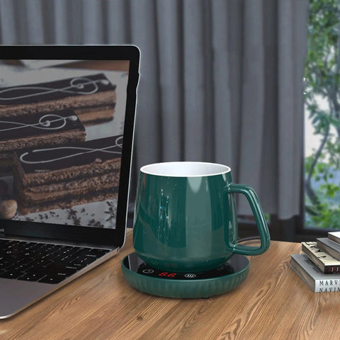 Tempered Glass Top Cup Warmer Pad With Digital Display And Auto Timer To Keep Your Morning Brew Piping Hot And Dodge The Cold Coffee Blues On Busy Weekdays, featuring a green ceramic mug on a warming pad next to a laptop.