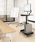 Heavy Lifter Mobile Workstation Cart With No Sweat Rolling Casters And Fully Adjustable Gas Spring Monitor Stand Plus Secure CPU Tray For Seamless Standing Desk Transitions In Matte Black in a classroom setting with a monitor and CPU.