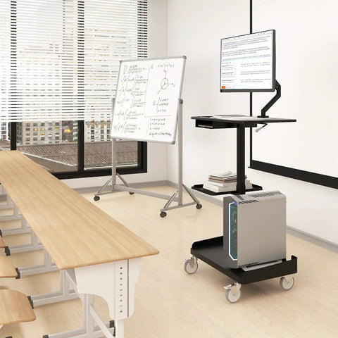 Heavy Lifter Mobile Workstation Cart With No Sweat Rolling Casters And Fully Adjustable Gas Spring Monitor Stand Plus Secure CPU Tray For Seamless Standing Desk Transitions In Matte Black in a classroom setting with a monitor and CPU.