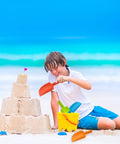 Boy playing with 4 Pack Beach Shovels For Kids 8 Inch Heavy Duty Plastic Sand Shovels next to sandcastle on beach