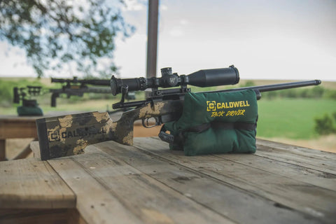 Rifle supported by TackDriver Gun Bag With One Piece Construction And Non Marring Surface For Outdoor Range And Hunting on a wooden table.