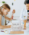 Acrylic Periodic Table With 83 Real Elements Inside Wooden Stand And Magnifying Glass in classroom with students and teacher.