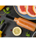 Bottle on table with Shrink Bands 50x60mm Black Pack Of 200 Tamper Evident Seal For Hot Sauce And Other Liquids, colorful fruits around.