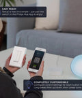 Person holding Battery Free Wireless Light Switch For Hue With 30 Foot Range Kinetic Wall Mount next to smartphone app.