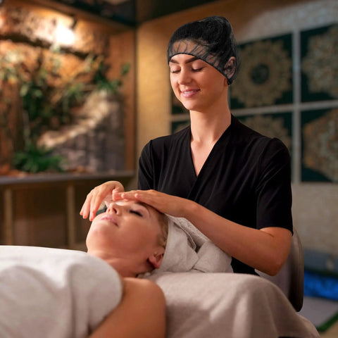 Therapist wearing Disposable No Fuss Hair Nets For Food Service Black Nylon 28 Inch Pack Of 100 during facial massage.